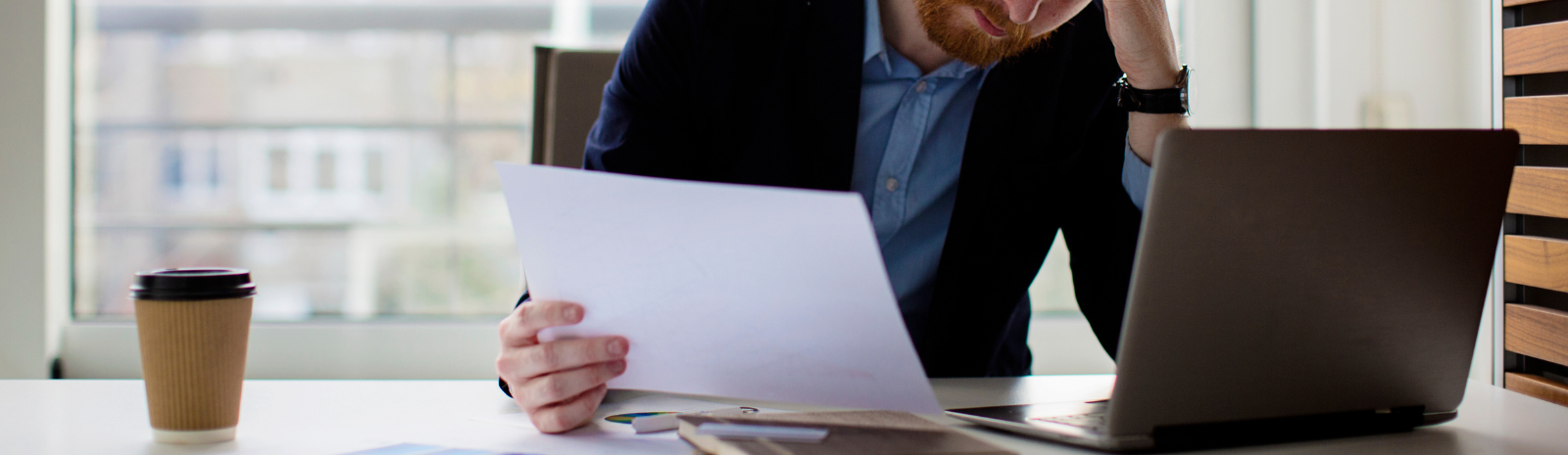 person at desk looking concerned looking at laptop and paperwork